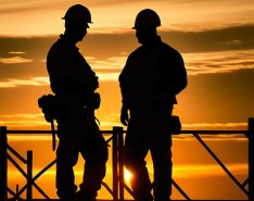 Two construction workers silhouetted against orange sky