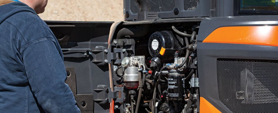 A construction worker looks at the inner working of a piece of machinery