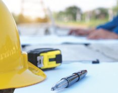 Hard hat and pen on a paper representing construction contracts / Adobe Stock